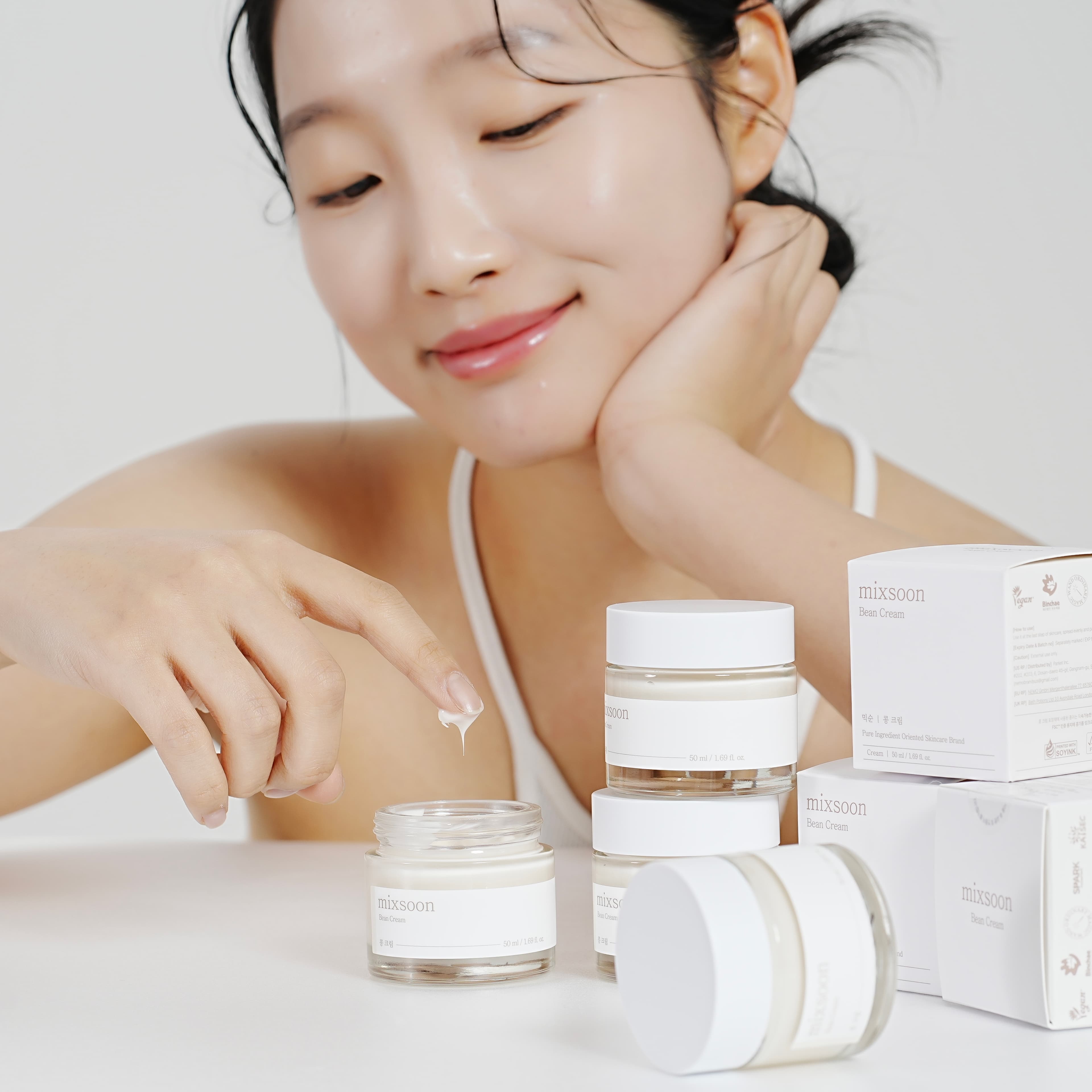 Femeie cu ten radiant aplicând mixsoon Bean Cream din borcan, alături de ambalajul produsului