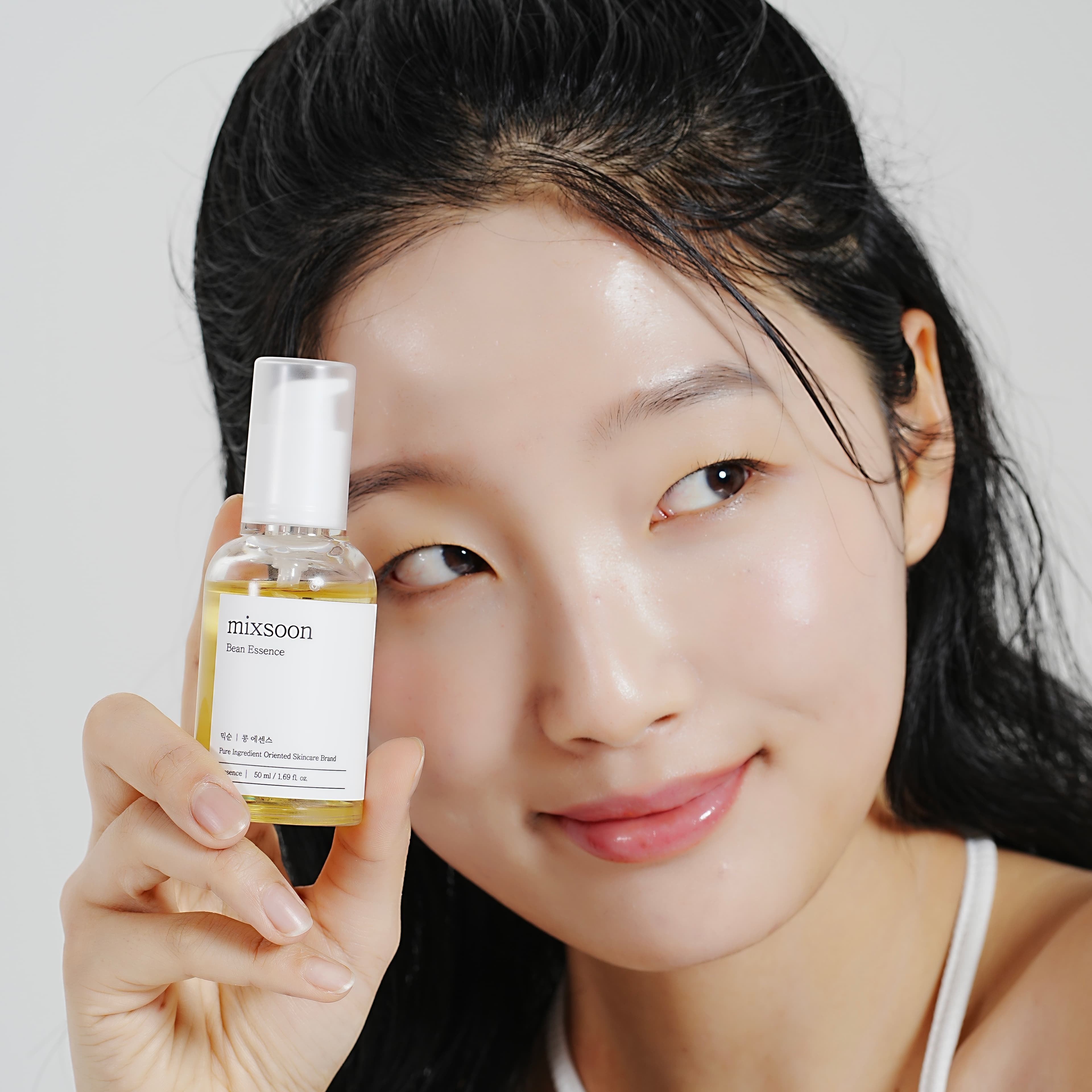 Model ținând o sticlă mixsoon Bean Essence lângă chip