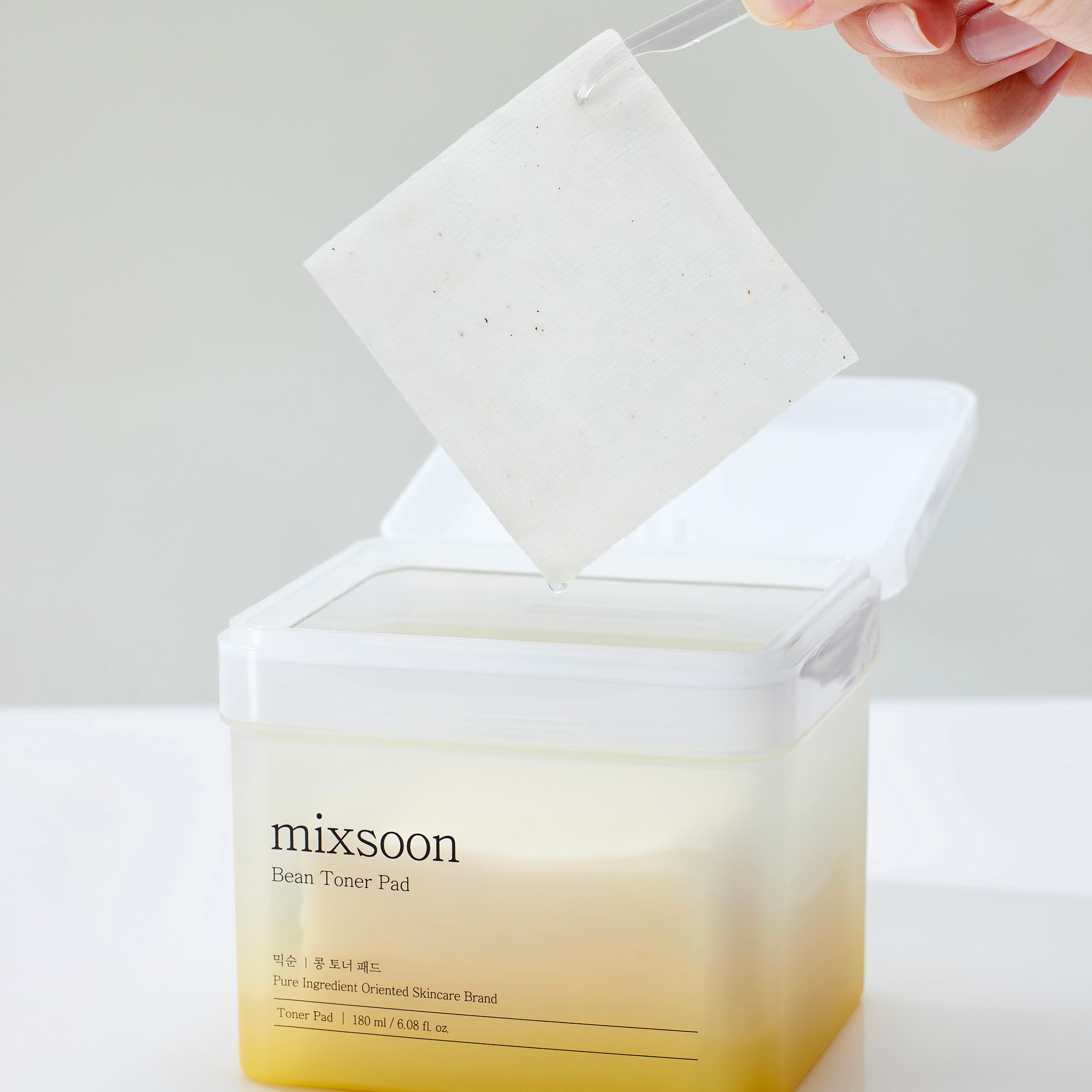 Un disc mixsoon Bean Toner Pad ridicat din recipient, cu esență care picură